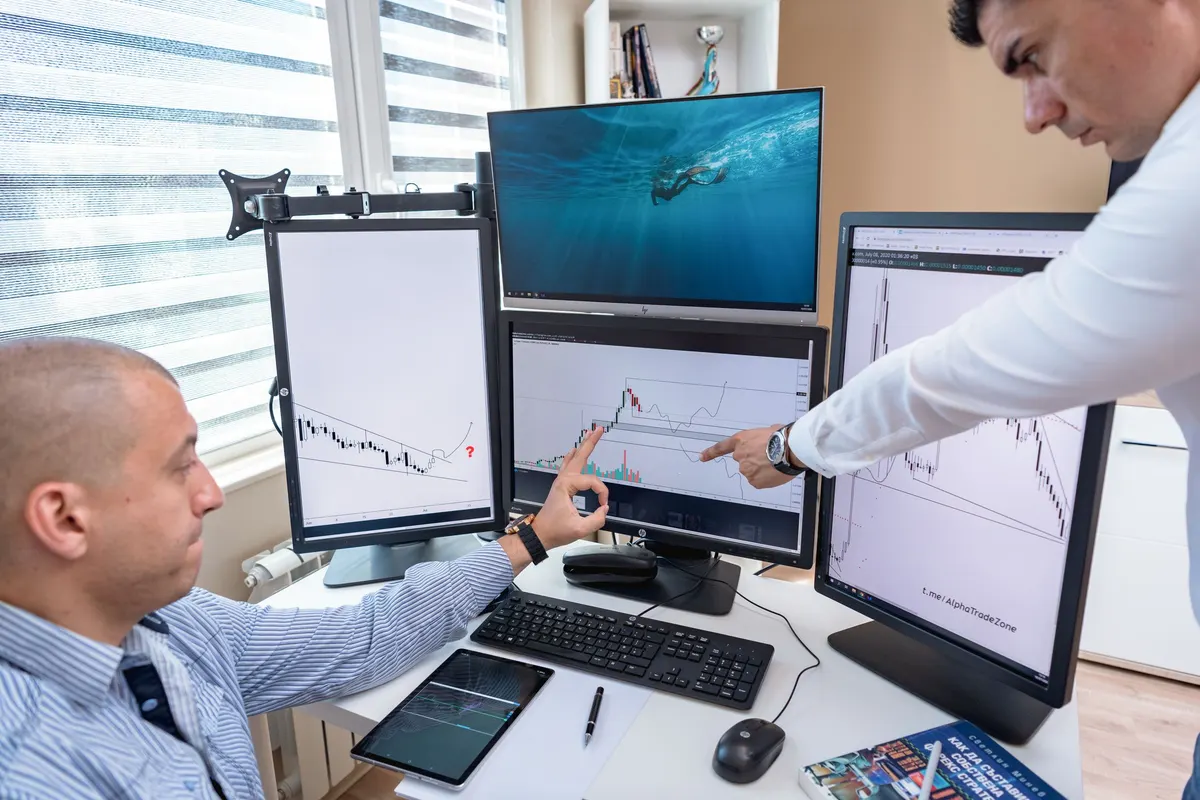 Two traders reviewing portfolio-level performance metrics on computer screens