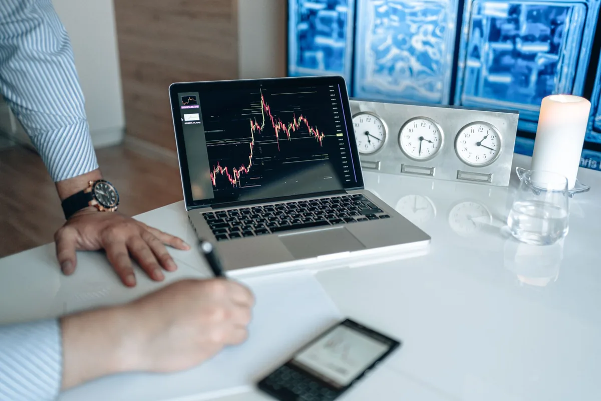 Trader analysing a stock chart on a laptop while reviewing trading notes